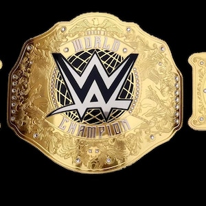 May include: A gold wrestling championship belt with a black and white logo that says "World Champion". The belt has two side plates with the name "Rhea Ripley" in black text on a gold background.