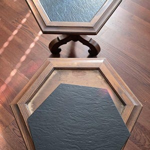 May include: Two hexagonal wooden side tables with dark slate tops. The tables have a dark brown finish and are set on a hardwood floor. One table is fully assembled, while the other has a slate top detached.