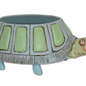 May include: A ceramic turtle planter with a light blue and green shell. The planter has a wide, shallow opening and four legs.