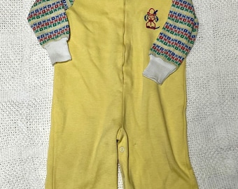 May include: Yellow baby sleeper with a zipper closure and a small embroidered dog wearing a hat on the front. The sleeves have a white and colorful geometric pattern.