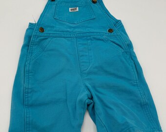 Może przedstawiać: Turkusowe dżinsowe ogrodniczki z regulowanymi ramiączkami i mosiężnym osprzętem. Kieszeń na szelkach ma małą etykietę "GUESS". Ogrodniczki w stylu szortów mają dwie przednie kieszenie i są wykonane z wytrzymałej mieszanki bawełny.