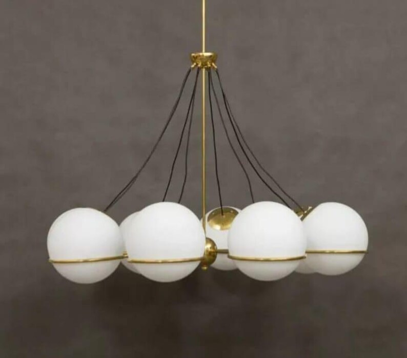 Pu&ograve; includere: Un lampadario moderno con pi&ugrave; luci a globo bianche con finiture color oro. Il lampadario ha un supporto centrale color oro e cavi neri che sospendono i globi. Il design &egrave; elegante e contemporaneo, adatto a vari stili di interni.