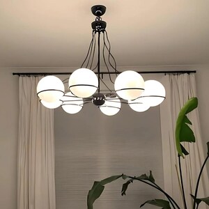 Pu&ograve; includere: Un moderno lampadario nero con sette paralumi sferici in vetro smerigliato. Ogni globo &egrave; circondato da una fascia metallica nera. L'apparecchio &egrave; appeso a un supporto a soffitto nero, creando un design di illuminazione contemporaneo.