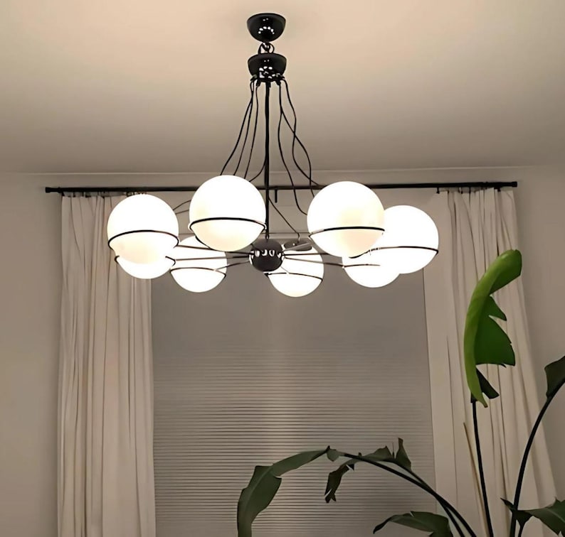 Pu&ograve; includere: Un moderno lampadario nero con sette paralumi sferici in vetro smerigliato. Ogni globo &egrave; circondato da una fascia metallica nera. L'apparecchio &egrave; appeso a un supporto a soffitto nero, creando un design di illuminazione contemporaneo.
