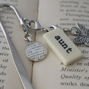 Pode incluir: Um marcador de página prateado com um amuleto que diz "deep-rejoice in contentment, joy /jɔɪ/ - assurance & confidence God is good" e outro amuleto que diz "aunt" com um amuleto de borboleta prateada.