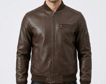 May include: A dark brown leather bomber jacket featuring a ribbed collar, cuffs, and hem. The jacket includes a full-length front zipper, a zippered chest pocket on the left side, and a small zippered utility pocket on the upper left sleeve.