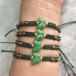 May include: Four green string bracelets with green butterfly charms. Each bracelet has gold and silver beads.