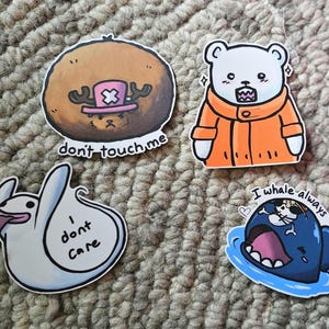 May include: Four colorful stickers with cartoon characters and text. The first sticker is brown with a pink and white hat and the text "don't touch me". The second sticker is white with an orange jacket and the text "I whale always love u". The third sticker is white with a ghost and the text "I don't care". The fourth sticker is blue with a whale and a small white character inside the whale's mouth.