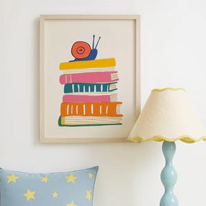 May include: A framed print depicts a stack of colorful books with a snail on top. A blue pillow with yellow stars rests on a bed. A light blue lamp with a cream-colored shade sits on a yellow nightstand.