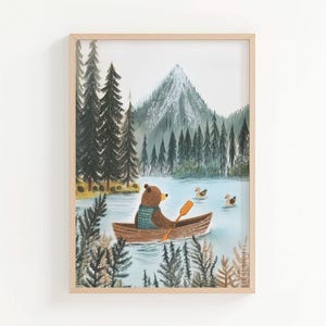 Puede incluir: Una impresión artística enmarcada representa un oso pardo en una canoa en un lago, remando con un remo naranja. El oso lleva un suéter azul y verde. El fondo muestra una montaña, árboles y dos patos.