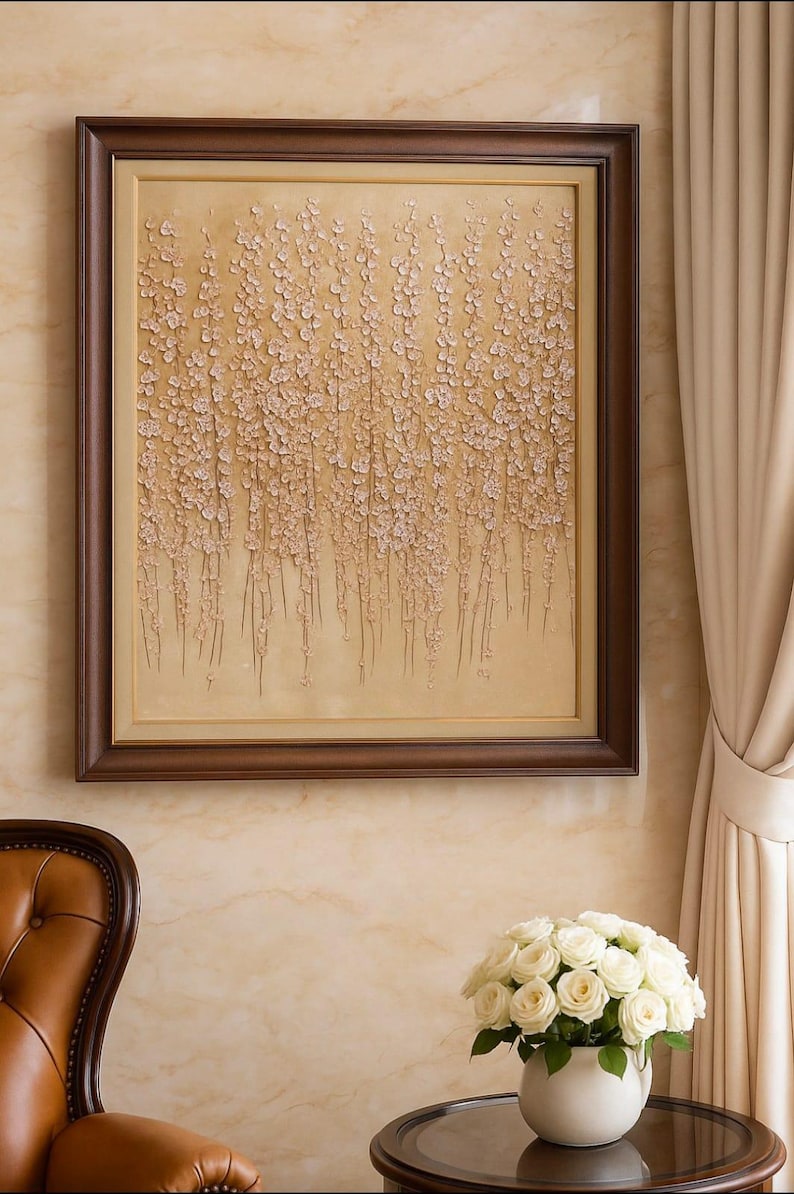 Puede incluir: Una obra de arte enmarcada con un fondo beige texturizado y elementos florales claros en cascada. La obra de arte est&aacute; encerrada en un marco de madera marr&oacute;n oscuro. Un ramo de rosas blancas se encuentra en un jarr&oacute;n blanco sobre una mesa.