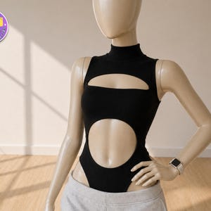 May include: A black bodysuit with a high neckline and cut-out design. The sleeveless garment features a large oval cut-out at the midriff and a smaller horizontal cut-out above the chest. The bodysuit is displayed on a mannequin.