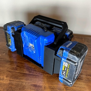 May include: A black 3D-printed power tool battery holder with a handle, holding a blue charger and two blue and black 24V MAX extended run batteries. The batteries are labeled with 4.0 Ah.
