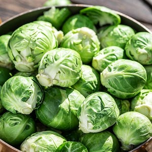 May include: A large, round, metallic cooking pot filled with numerous fresh, raw Brussels sprouts. The sprouts are vibrant green, tightly packed, and spherical in shape, showcasing their layered, leafy texture within the deep, circular container.