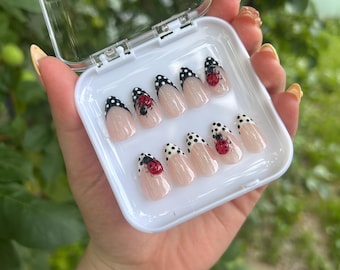 Peut inclure: Un ensemble de dix faux ongles dans un étui en plastique transparent. Les ongles sont de couleur nude avec des pois noirs et des motifs de coccinelles. Les ongles sont de forme ovale et ont une finition brillante.