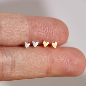 May include: Three pairs of small heart-shaped stud earrings. The earrings are in silver and gold.