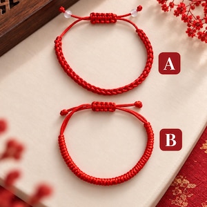 May include: Two red cord bracelets with adjustable sliding knots. Bracelet A features a braided pattern with two small translucent beads at the ends. Bracelet B features a tightly coiled, round cord design. Both are labeled with red square icons.