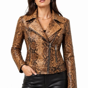 May include: Brown snakeskin-patterned leather jacket with a notched collar and asymmetrical zipper closure. The jacket has two zippered pockets and long sleeves. The model is wearing black pants.