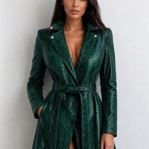 May include: A long, emerald green coat with a snakeskin pattern. The coat features a belted waist, a notched collar, and gold-colored buttons. The coat is open in the front, revealing a deep V-neckline.