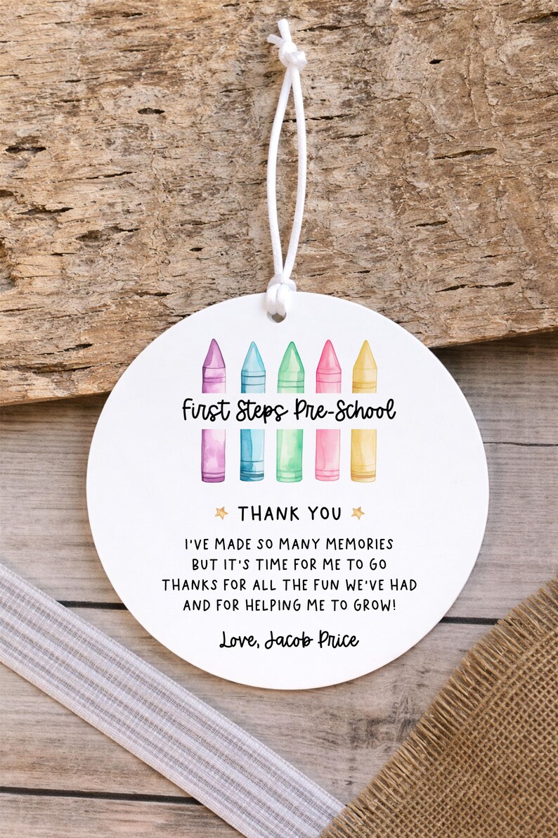 May include: A round white ornament with a white string featuring a watercolour illustration of five colourful crayons and the text First Steps Pre-School, THANK YOU, I'VE MADE SO MANY MEMORIES BUT IT'S TIME FOR ME TO GO THANKS FOR ALL THE FUN WE'VE HAD AND FOR HELPING ME TO GROW! Love, Jacob Price.