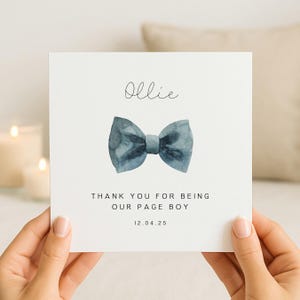 May include: A square white greeting card featuring a watercolor illustration of a blue bow tie in the center. The text reads Ollie at the top, Thank you for being our page boy in the middle, and the date 12.04.25 at the bottom in black font.