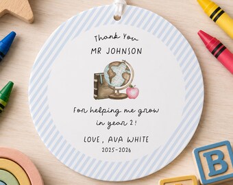 May include: A round white ceramic ornament with a light blue diagonal striped border. The center features a watercolor illustration of a globe, a book, and an apple, with the text: Thank You MR JOHNSON For helping me grow in year 2! LOVE, AVA WHITE 2025-2026.