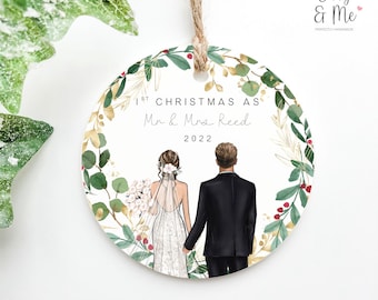 May include: A round, white Christmas ornament with a green and gold floral wreath design. The ornament features a bride and groom in silhouette, with the text "1st Christmas as Mr & Mrs Reed 2022".