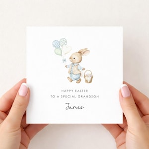 May include: A white Easter greeting card featuring a watercolor illustration of a bunny holding balloons and a basket of eggs. The text reads "Happy Easter to a special grandson" with the name "James" below.