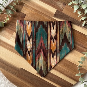 May include: A brown, teal, orange, and pink patterned bandana with a geometric design. The bandana is on a wooden surface.