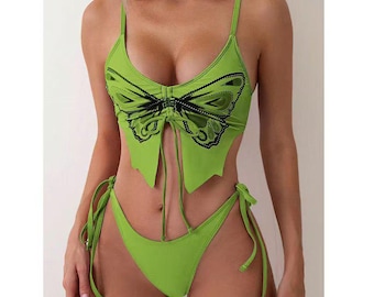 Könnte beinhalten: Ein limettengrünes Bikini-Set mit Schmetterlingsdesign. Das Oberteil hat eine Schmetterlingsgrafik und verstellbare Träger. Die Hose ist passend grün mit Bindebändern an den Seiten. Die Bademode ist aus glattem, wahrscheinlich dehnbarem Material.