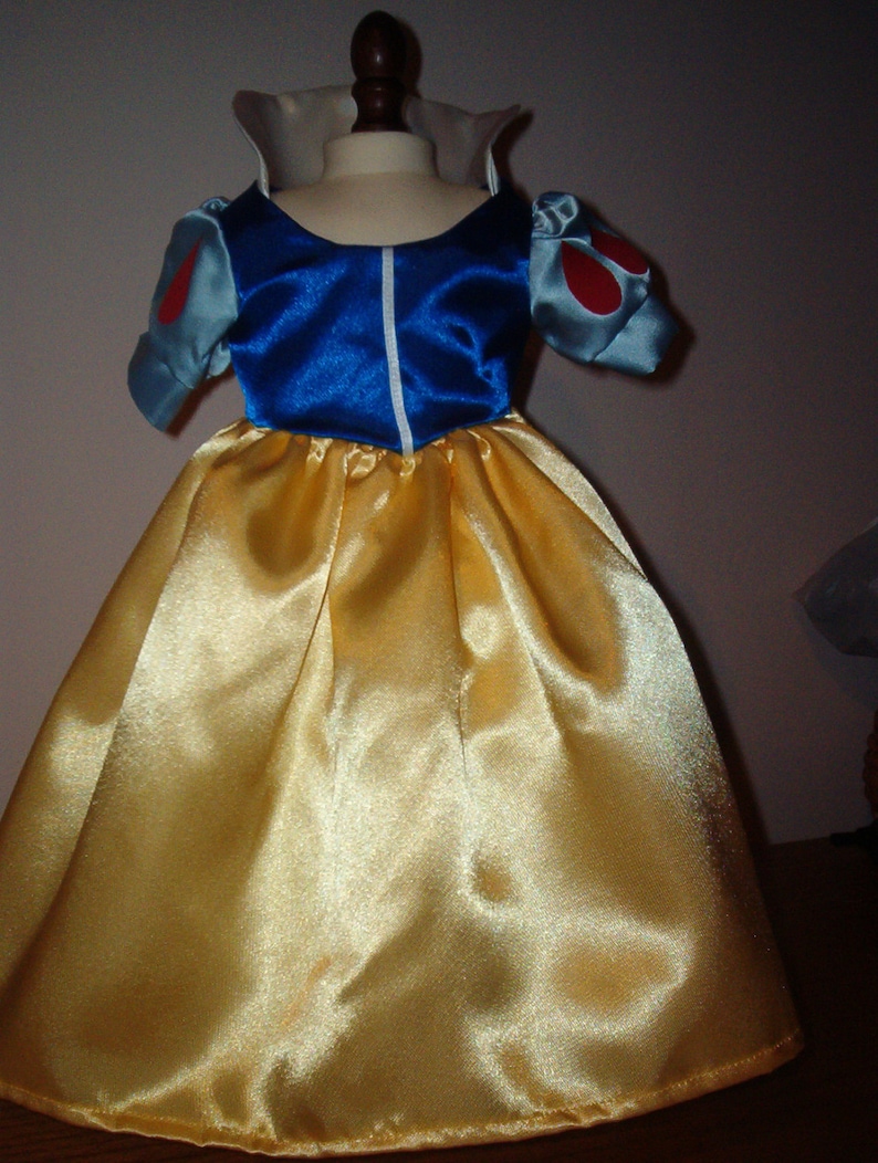 K&ouml;nnte beinhalten: Ein gelbes Satinkleid mit einem blauen Satin-Mieder und wei&szlig;en Besatz. Das Kleid hat Puff&auml;rmel mit roten Akzenten.