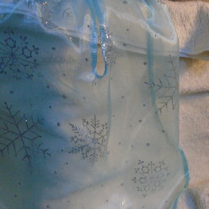 Peut inclure: Un tissu de tulle bleu clair avec des flocons de neige argent&eacute;s. Le tissu a une texture transparente et d&eacute;licate.