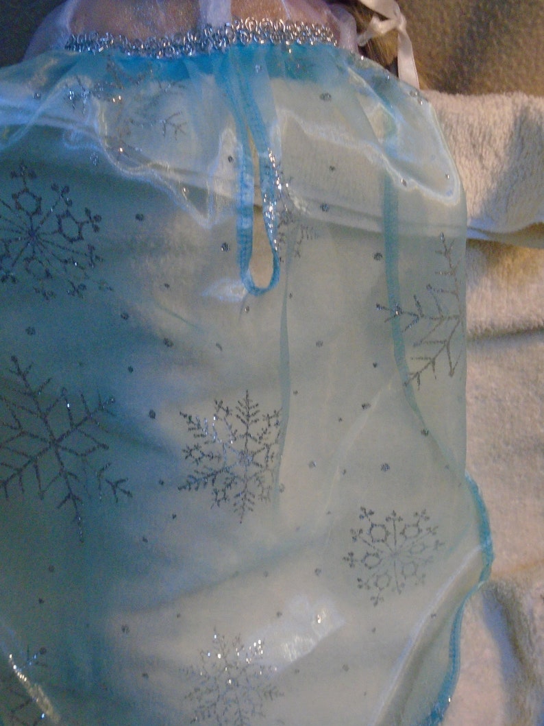 Peut inclure: Un tissu de tulle bleu clair avec des flocons de neige argent&eacute;s. Le tissu a une texture transparente et d&eacute;licate.