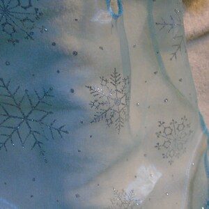 Peut inclure: Un tissu transparent bleu clair avec des flocons de neige argent&eacute;s. Le tissu est translucide et a une texture d&eacute;licate et a&eacute;rienne.