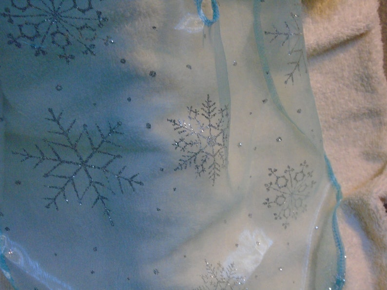 Peut inclure: Un tissu transparent bleu clair avec des flocons de neige argent&eacute;s. Le tissu est translucide et a une texture d&eacute;licate et a&eacute;rienne.
