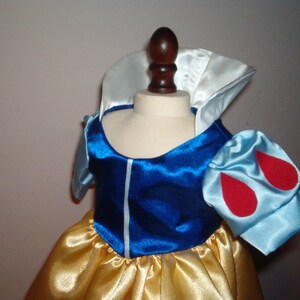 K&ouml;nnte beinhalten: Ein blaues und wei&szlig;es Satin-Kleid mit roten Akzenten. Das Kleid hat einen wei&szlig;en Kragen und Puff&auml;rmel mit roten Tropfenformen. Der Rock ist aus gelbem Satin.