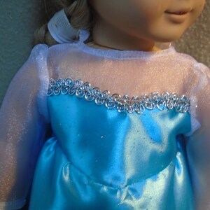 Peut inclure: Une robe bleue avec une bordure argent&eacute;e et des manches blanches transparentes. La robe a une texture scintillante.