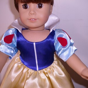 K&ouml;nnte beinhalten: Eine Puppe, die ein blaues und wei&szlig;es Kleid mit roten Akzenten tr&auml;gt. Das Kleid hat einen wei&szlig;en Kragen und Puff&auml;rmel. Die Puppe hat braunes Haar und blaue Augen.