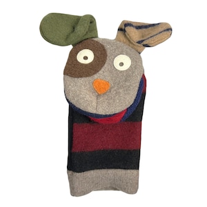 May include: A gray felt puppet with a brown and white face, orange nose, and green and brown ears. The puppet is wearing a red, black, and gray striped scarf.