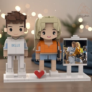 May include: A custom building block set featuring two stylized figures on a white base. The left figure has brown hair and a white jersey with the text DELLE. The right figure has blonde hair and an orange top. A photo frame displays a couple.