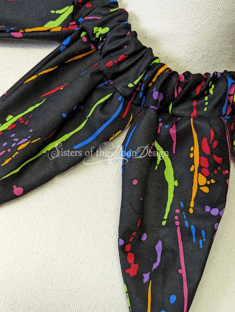 May include: Black fabric with a colorful paint splatter design. The fabric has a gathered elastic band at the top.