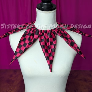 May include: A black and pink checkered fabric collar with pointed edges. The collar is on a white mannequin. The text "Sisters of the Moon Design" is visible in the background.