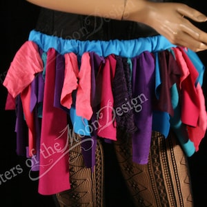May include: A colorful skirt made of strips of fabric in shades of pink, purple, blue, and teal. The skirt is gathered at the waist and has a blue elastic waistband.