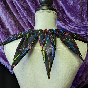 May include: A black fabric collar with a colorful paint splatter design. The collar has a gathered elastic band at the back.
