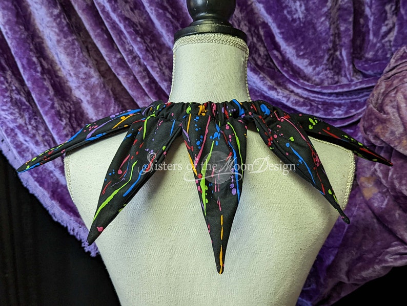 May include: A black fabric collar with a colorful paint splatter design. The collar has a gathered elastic band at the back.