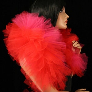 May include: A red and pink tulle boa with a ruffled texture. The boa is worn around the neck of a mannequin.