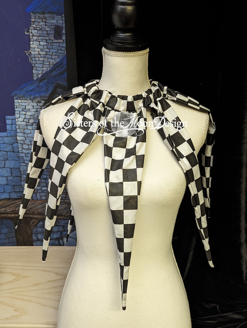 May include: A black and white checkered fabric collar with long, pointed ends. The collar is on a white dress form. The text "Sisters of the Moon Design" is visible on the collar.