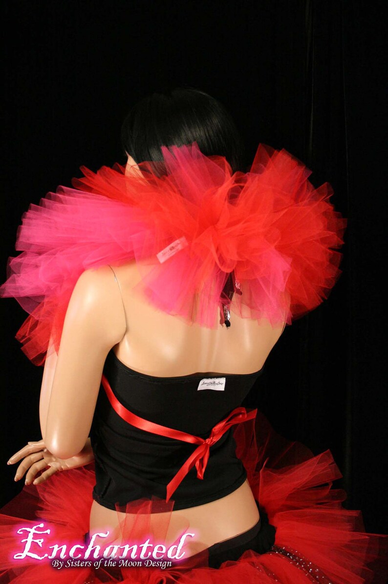 May include: A red and pink tulle tutu skirt with a black top and a red ribbon. The skirt is layered and has a fluffy texture. The top is a simple black tank top with a red ribbon tied around the waist. The model is wearing the skirt and top and is standing in front of a black background.