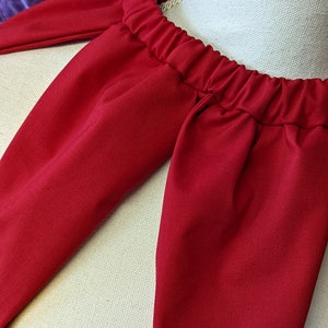 May include: Red fabric cape with a gathered neckline. The cape is made of a soft, smooth fabric.