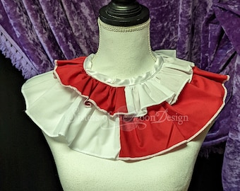May include: A white and red ruffled collar with a white satin ribbon. The collar is on a white mannequin bust. The background is a purple velvet curtain.